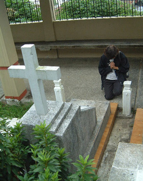 両親の墓前で祈りを捧げる寺岡マリエさん。墓石の周囲ではツツジが茂る
