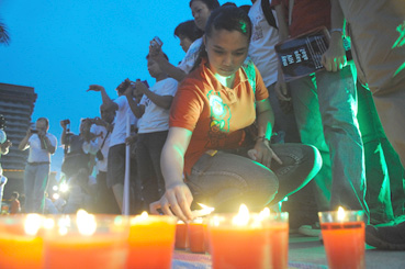 エイズによる死亡者を追悼する集会で、キルトの回りにロウソクをともす女性参加者=28日午後6時半ごろ、首都圏マニラ市で写す