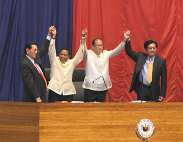 両手を挙げて当選を喜ぶアキノ次期大統領(右から2人目)とビナイ次期副大統領(同3人目)。右端はノグラレス下院議長、左端はエンリレ上院議長=9日午後4時ごろ、首都圏ケソン市の下院本会議場で写す