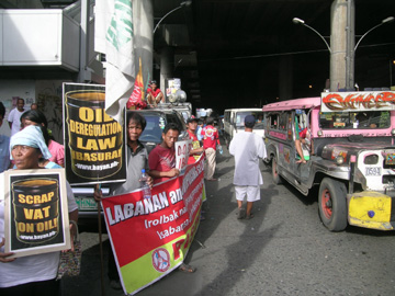 運行を続ける多数のジプニーの横で抗議するスト参加者ら=19日午後3時半ごろ、首都圏ケソン市クバオのアウロラ通りで写す