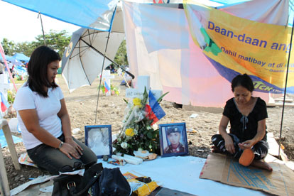 故エメルソン・ツガス上等兵の墓前で沈痛な面持ちを見せる妻のロニラ(左)さんとエメルソンさんの母親=1日午後3時半ごろ、首都圏タギッグ市の英雄墓地で写す