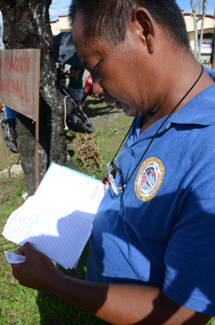 集団埋葬地となった教会前広場で、犠牲者名などが書かれた帳面に視線を落とすランタホ議長=12月2日、レイテ州パロ町で写す