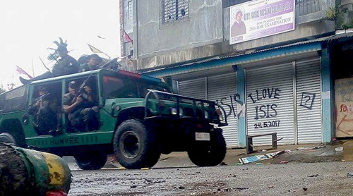 「イスラム国(IS)愛している」と落書きされたシャッターの前をパトロールする警官ら=29日正午ごろ、ミンダナオ地方南ラナオ州マラウィ市でクリサント・バリエタ撮影