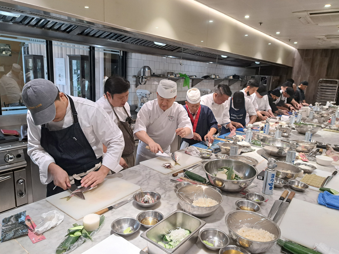 あじの三枚おろしの方法を説明する小川洋利氏(左から3人目)=6日午後3時半ごろ、澤田公伸撮影